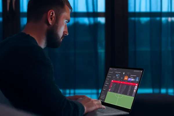 4777BAT Mobile App — Your complete hub for casino and sports A man focused on his laptop with live stats in the background, highlighting the dedicated sports and gaming features of the 4777BAT mobile app.