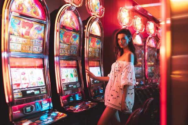 4777BAT Slots — Thousands of exciting themes and jackpots A stylish woman beside vibrant slot machines displaying glowing sevens, showcasing the variety of top slots at 4777BAT.