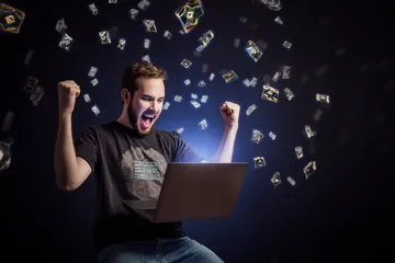 A man celebrating a winning moment on his laptop while gaming symbols float around him, capturing the excitement of 4777BAT games.