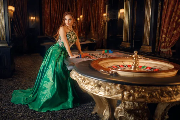 4777BAT — A high-class gaming experience without limits A woman in a luxurious green gown next to an ornate roulette wheel, capturing the upscale casino mood of 4777BAT.